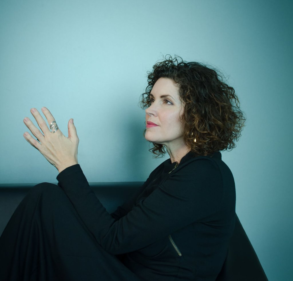 Photo of Crista Cloutier in blue background, sharing why she built the working artist academy