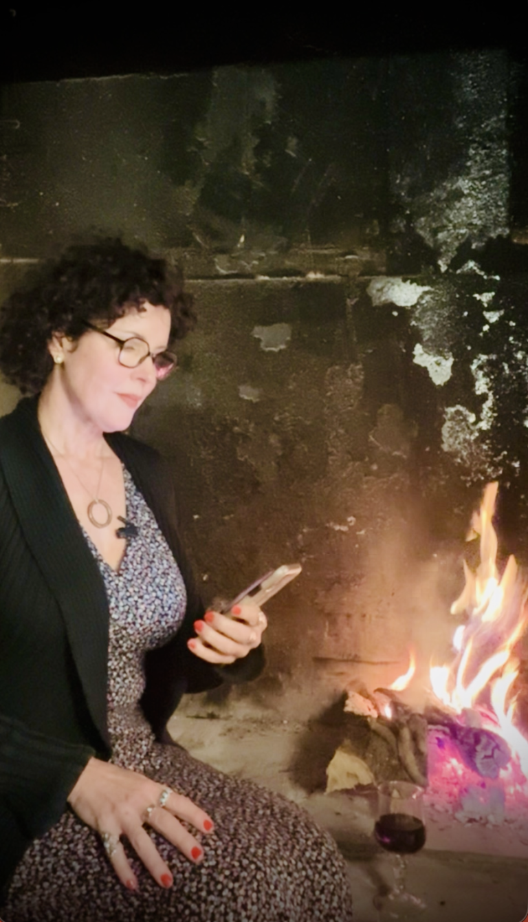 Crista sitting by the fireplace reading and responding to a hate mail about the working artist academy