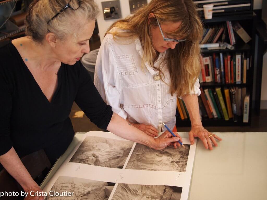 Two artists concentrating on an artwork, one scribbling with a pencil while the other observes.