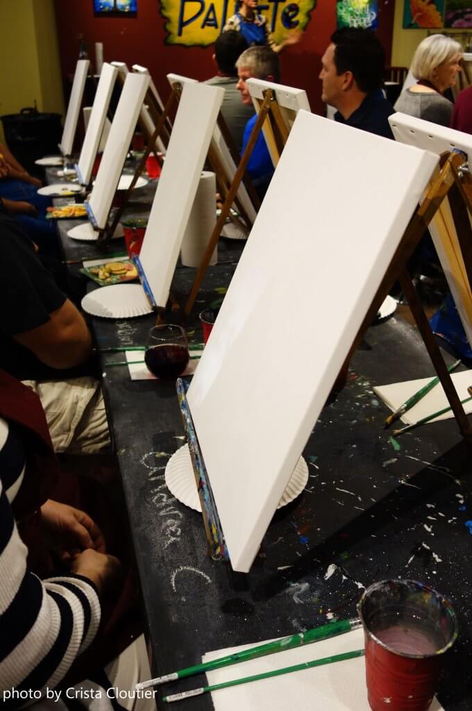 Artists seated at tables with canvases in a painting workshop photographed by Crista Cloutier.